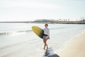 Beautiful young girl walks along the shore with a surfboard. Lifestyle concept. 