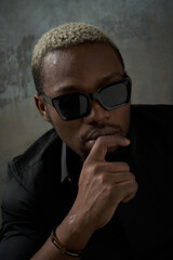 Obraz premium Close-up face studio portrait of young stylish glamor handsome african man with short white hair in black silk shirt and sunglasses posing against grey concrete wall