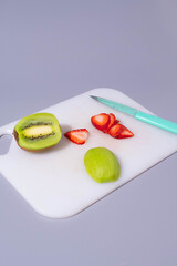Slice of kiwi and strawberry on cutting board with green knife