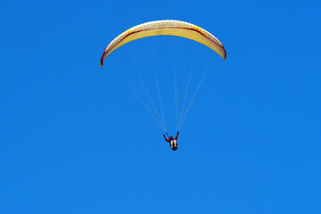 The athlete is flying a paraglider. Yellow paraglider against the blue sky on a clear sunny summer day