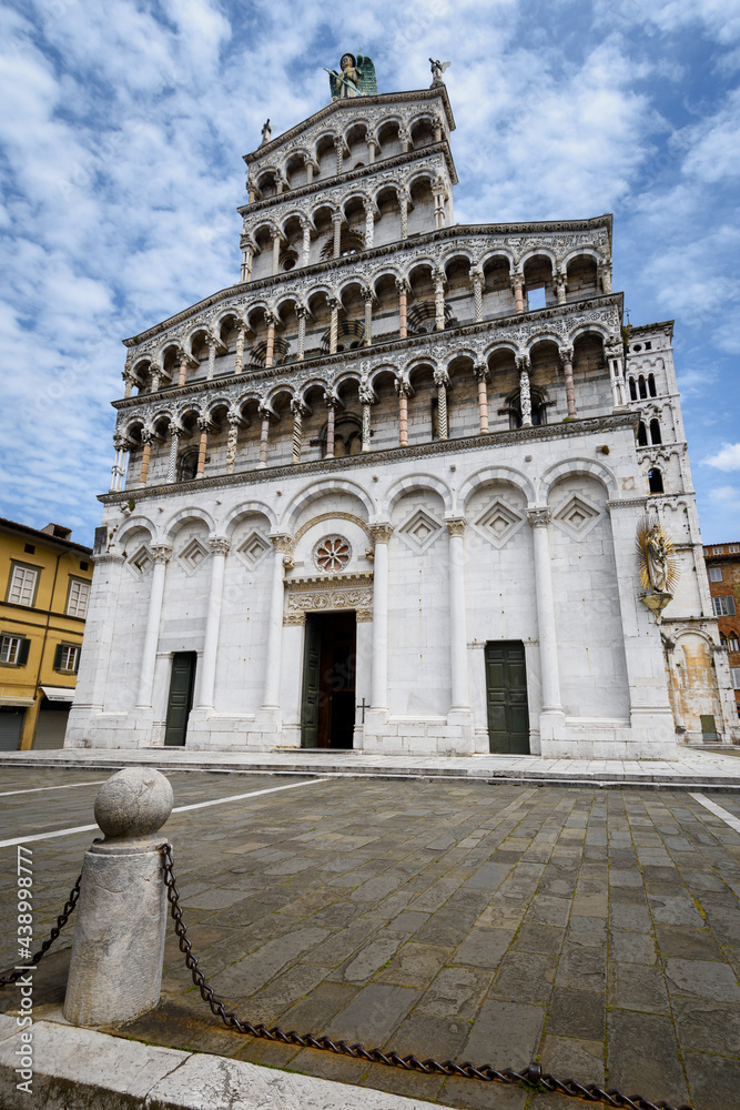 Wall mural Church and square of San Michele (Saint Michael) in Lucca, Tuscany (Italy). View of the white marble facace, with arches and decorated columns over blue cloudy sky