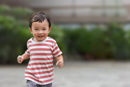 Portrait Of An Asian Boy (toddler) Running Toward And Smiling With Happy And Fun Face While Playing Outdoor. A Child Wear Striped Shirt In Red And White Color. Head And Hair Is Wet By Sweat.