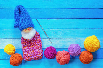 Hobby and knitting concepts.  Multi-colored balls of wool on blue rustic table. Funny knitted gnome...