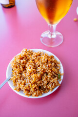 Rice dish top with a beer on a pink table.