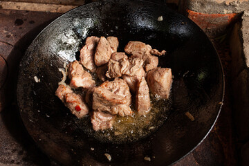 Frying round fried cubes with beef bottom in a cast-iron skillet, grilling meat in olia on the fire