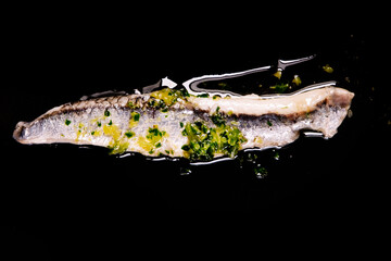 Piece of anchovies with garlic, parsley and oil on a black background.