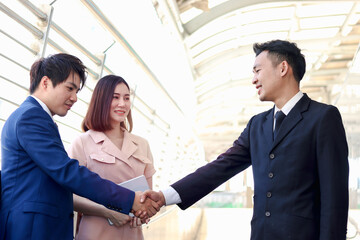 Two successful businessmen shaking hands after sign contract, businesswomen appreciating the good result, businesspeople meeting at outside office in downtown city.
