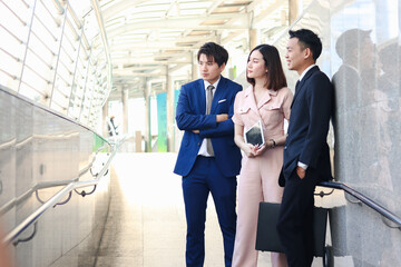 Portrait of three Asian businessman and businesswoman confidential standing in the city, businesspeople talking about job while walking in downtown city.