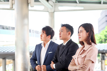 Portrait of three Asian businessman and businesswoman confidential standing in line and looking the same way, businesspeople talking about job while walking in downtown city.