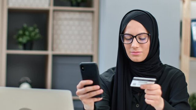 Smiling Muslim woman use smartphone application online shopping card payment goods from internet