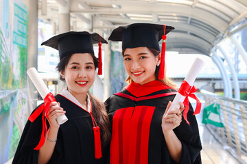Portrait of two happy smiling graduated students holding  certificate, young beautiful Asian women looking at camera so proud on their commencement day, people celebrating successful education on grad