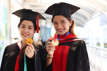 Portrait of two happy smiling graduated students holding  gold medal award, young beautiful Asian women looking at camera so proud on their commencement day, people celebrating successful education on