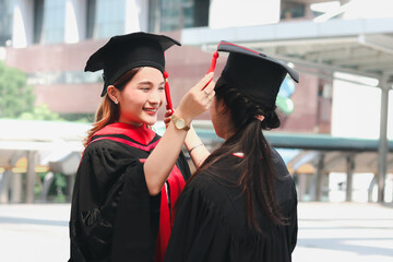 Two happy graduated women students touching square academic hat cap of each other, people...