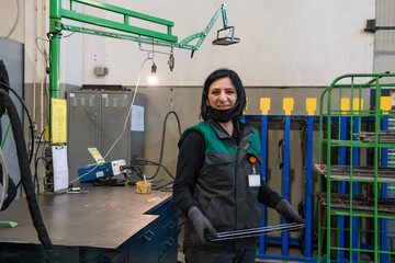 a portrait of a woman in uniform carrying a piece of metal and preparing it for the final part of production