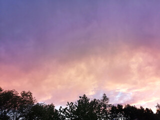 Beautiful colorful acid sunset sky view. Purple, pink, orange and blue sunset cloud sky with trees.