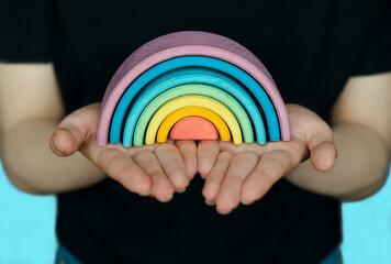 Hands Holding A Rainbow. A beautiful, colorful, wooden rainbow in the hands of a young girl on a blue background. A symbol of peace, happiness, love, and hope. Everything will be fine. Banner design