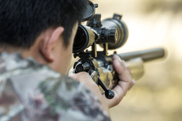 Camouflage sniper shooting rifle by looking through a scope hunting.
