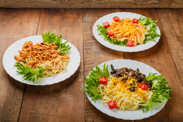 Three plates with different pasta on a wooden table.