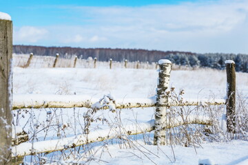 snow covered log fence on the field in winter 