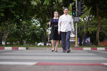 Blind person Asian woman with white cane crossing street walking on crosswalk with the sighted...