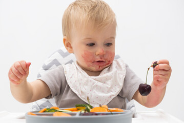 Adorable caucasian baby about 1 year old, eating fresh vegetables, fruits at high chair....