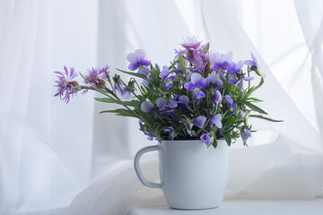 Delicate bouquet of flowers pansies in a cup on the windowsill