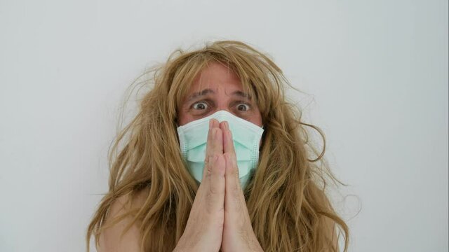 Man with long blond hair wearing a protective mask on his face and moving hysterically, man tearing off his protective mask and blonde wig in a gesture of rebellion during covid time