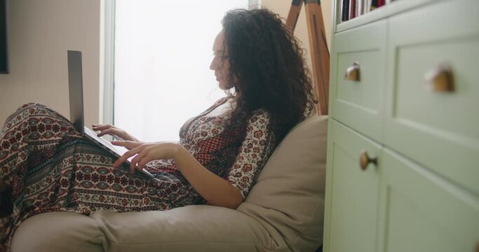 A young woman in dress typing on a computer, working from home. Slow motion, handheld, medium shot. 