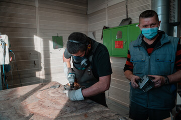 Industrial work during a pandemic. Two men work in a heavy metal factory, wearing a mask on their face due to a coronavirus pandemic