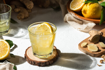 Detox lemon and ginger drink, with ice and a slice of lemon inside the glass, as an immune boosting and weight loss drink on a white textured surface, hard light