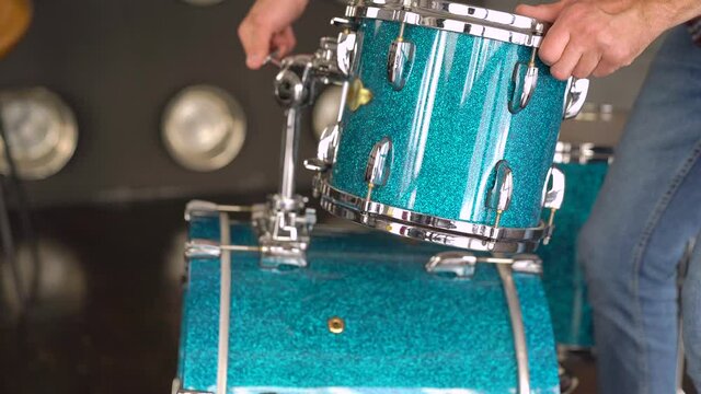 Caucasian male sets the blue drum to the drum-set to start the rehearsal