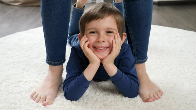 Portrait of happy smiling little boy lying on carpet between mother's feet