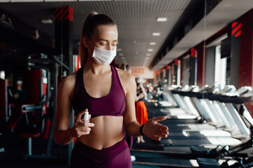 Fototapeta na wymiar A fit woman in a face mask to avoid the spread of coronavirus is doing bicep curls with dumbbells. A sporty girl in a surgical mask is posing during the arms workout in the gym.