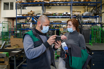 Industrial workers with face masks protected against corona virus discussing about production in factory. People working during COVID-19 pandemic.