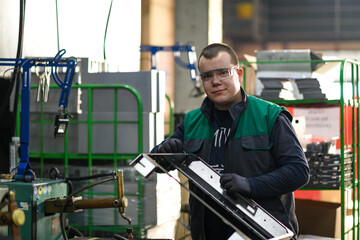 a uniformed worker working in a modern metal production and processing factory assembles parts of a...