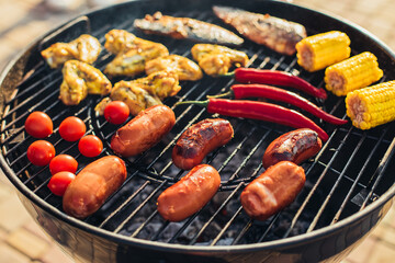 Delicious assorted grilled meat and sausages, with grilled vegetables with smoke and flame outdoors in the park in