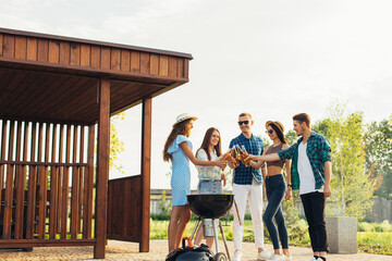 Barbecue time, a group of young friends preparing a barbecue outdoors in nature, drinking drinks and having fun