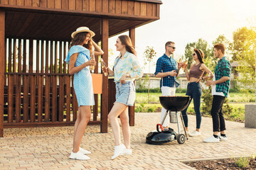 Young friends have fun frying meat, enjoying barbecue, with drinks, on a sunny day in nature