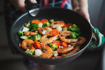 Woman cooking vegetables and shrimps on pan