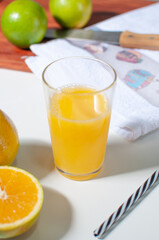 Orange juice in a glass on a white table with oranges, a knife and a white cloth