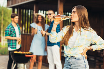 young woman, with a group of students friends doing barbecue, with beer drinks, having a rest on a sunny day, picnic, summer vacation