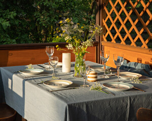 Served table at wooden summer terrace. Country house in Russia. Everning meal. Simple glasses, plates and wild flower. Blue and yellow