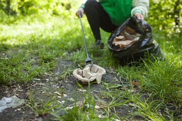 Selective focus on paper cup holder in the grass, volunteer picking trash in the forest on background