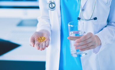 shot of doctor's hands holding pills and glass of water at clinic.