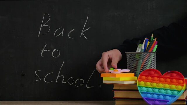 Written in chalk on the blackboard Back to school. There are books and school supplies. Popit. Simple dimple. Pop it. 4K