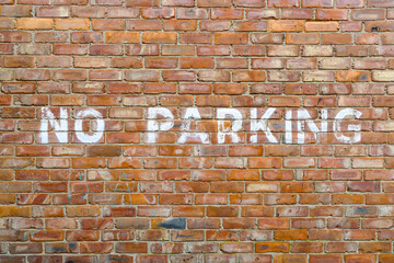 A white No Parking stencilled sign painted on a red brick wall