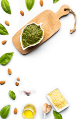Green pesto sauce made of basil, almonds, garlic, parmesan cheese and olive oil, in a leaf-shaped porcelain bowl and a small wooden table, on a pure white surface with copy space