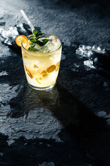 Iced kumquat drink with peppermint as an immune boosting and vitamin C source on a textured concrete replica surface, condensation by the glass and ice melting, hard light.
