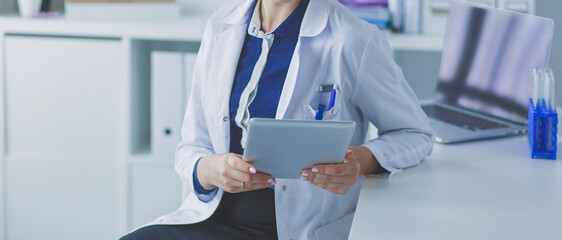 Portrait of woman doctor at hospital corridor, holding tablet computer, looking at camera, smiling