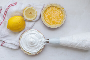Making of mini lemon meringue pies in tartlet forms, one with, one without meringue, and lemon curd, and a piping bag full of meringue